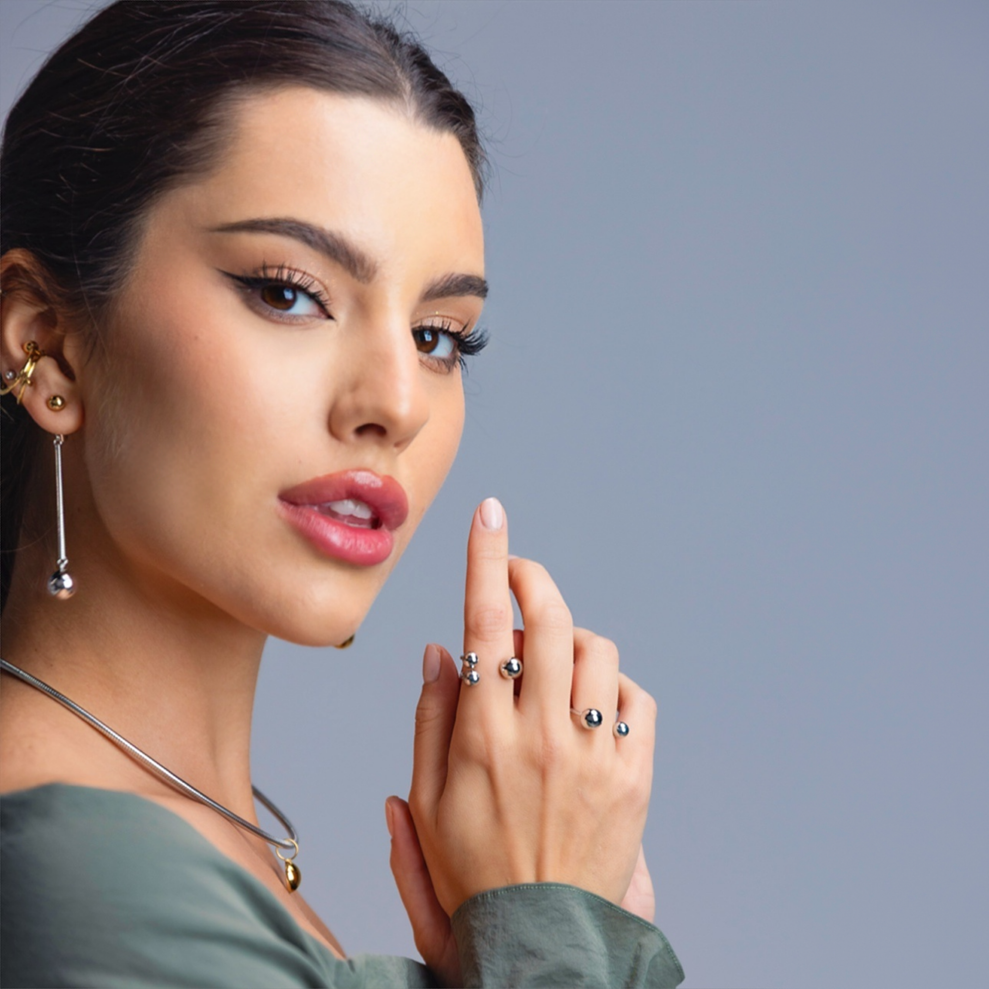 Woman wearing jewelry including earrings, a necklace, and rings on a gray background