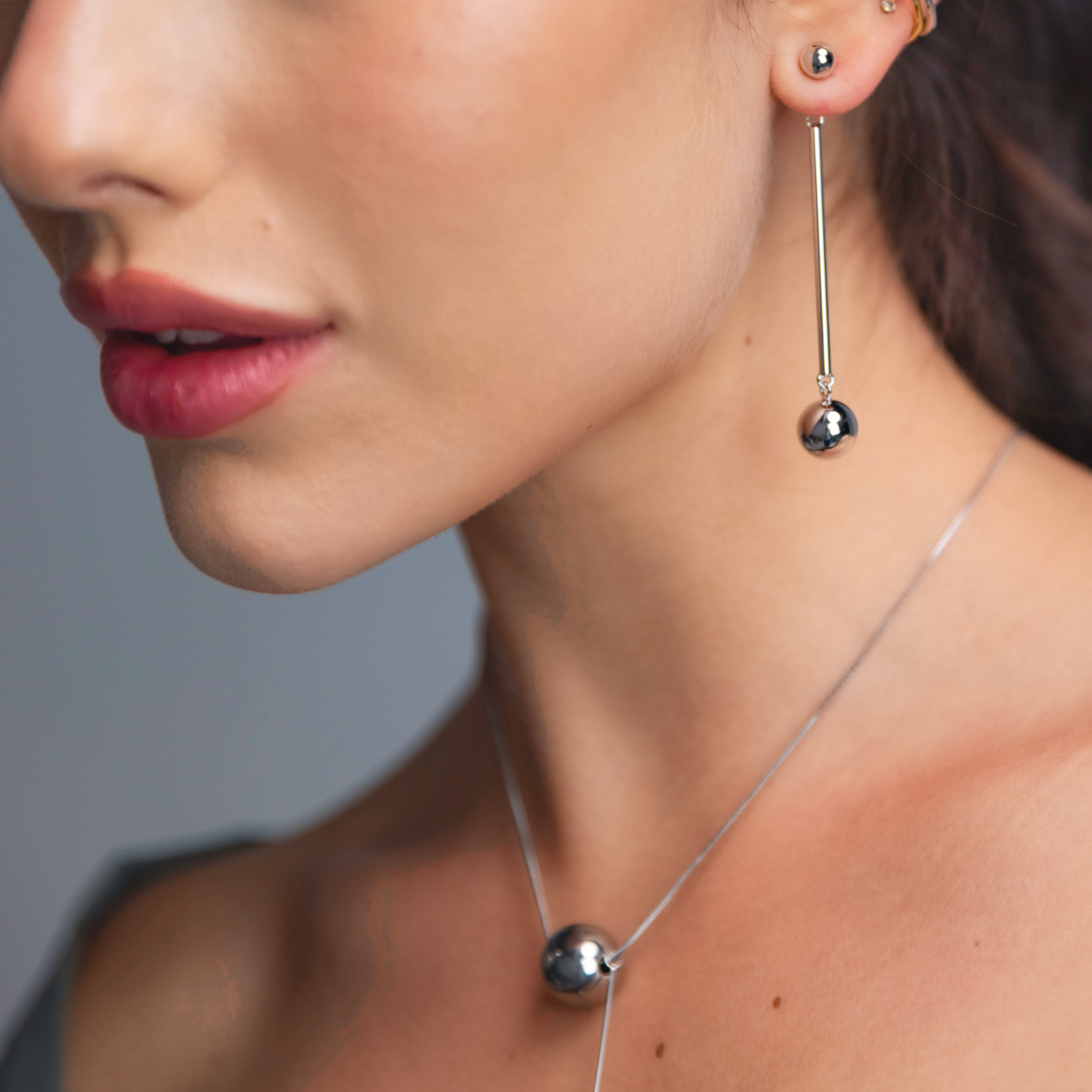 Close-up of a woman's ear wearing silver sphere drop earrings and a silver necklace.