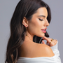 Side profile of a woman wearing a gold sphere drop earring, a gold sphere pendant necklace, and a gold open-band ring, styled in an off-shoulder white top.