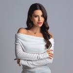 Woman wearing a gold sphere pendant necklace, gold drop earrings, and a gold open-band ring, styled in an off-shoulder white top against a neutral background.