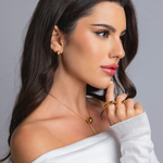 Side profile of a woman wearing gold sphere stud earrings, a gold sphere pendant necklace, and a gold open-band ring.