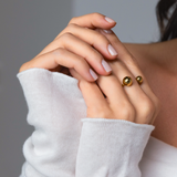 Close-up of hands wearing a gold open-band ring with polished spheres, styled with a soft white knit sleeve.